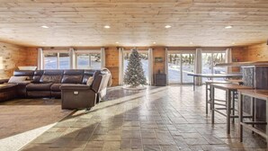 A log cabin interior with a leather sofa, a stone-tiled floor, a Christmas tree, and a bar area. - Updated 4BR, Game Room/Bar, Private, Near Gunstock (Gilford)