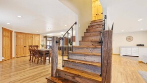 A spacious living area with a wooden staircase, a dining table, and a kitchen in the background. - Updated 4BR, Game Room/Bar, Private, Near Gunstock (Gilford)