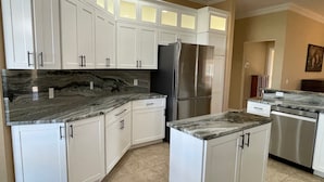 A kitchen with white cabinets, a stainless steel refrigerator, and a marble countertop.
