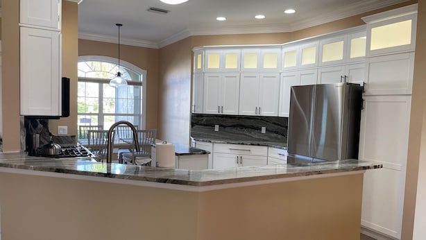 A modern kitchen with white cabinetry, a stainless steel refrigerator, and a marble countertop.