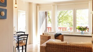 A bright room with wicker furniture, a dining table with chairs, and large windows with curtains. - Immenhagen (Malente)