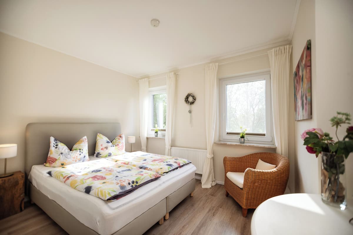 Un dormitorio con cama, una silla, una mesa y una ventana.