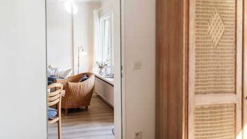 Een gang die leidt naar een kamer met een rieten stoel, een lamp en een raam met uitzicht.