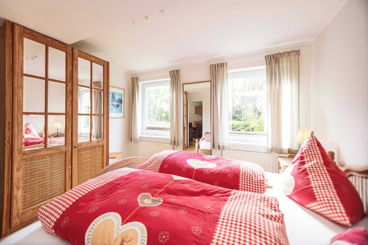Un dormitorio con dos camas, un armario de madera y ventanas amplias.