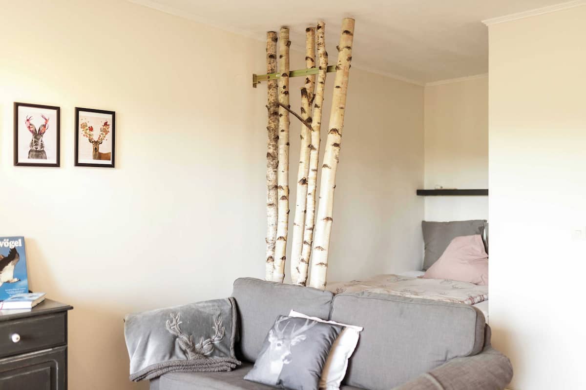 Una habitación con un sofá gris, una cama con colcha gris y rosa, y una estantería empotrada con dos cuadros enmarcados.