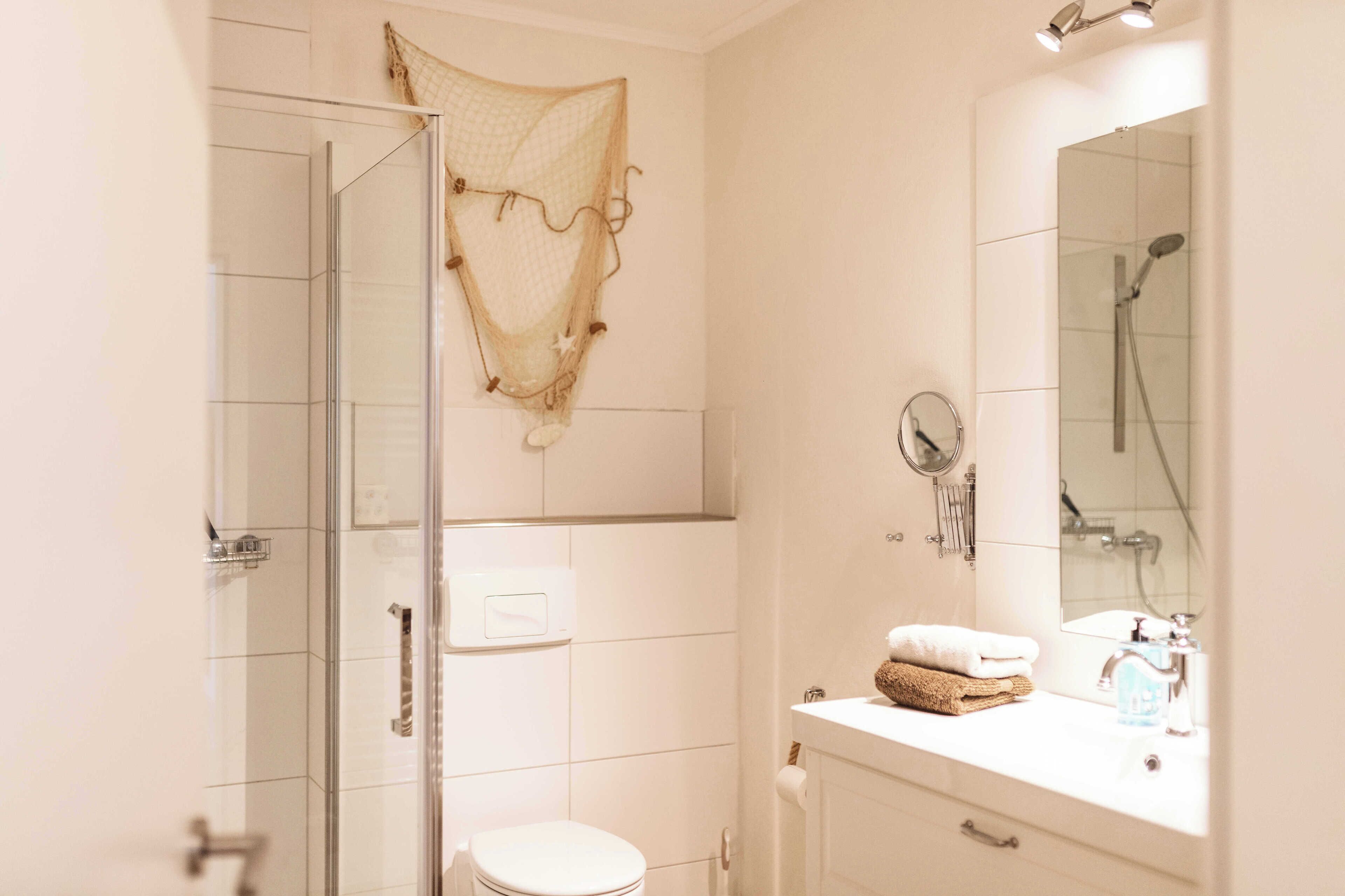 A bathroom with a glass shower enclosure, a toilet, a sink with a mirror, and a towel rack.