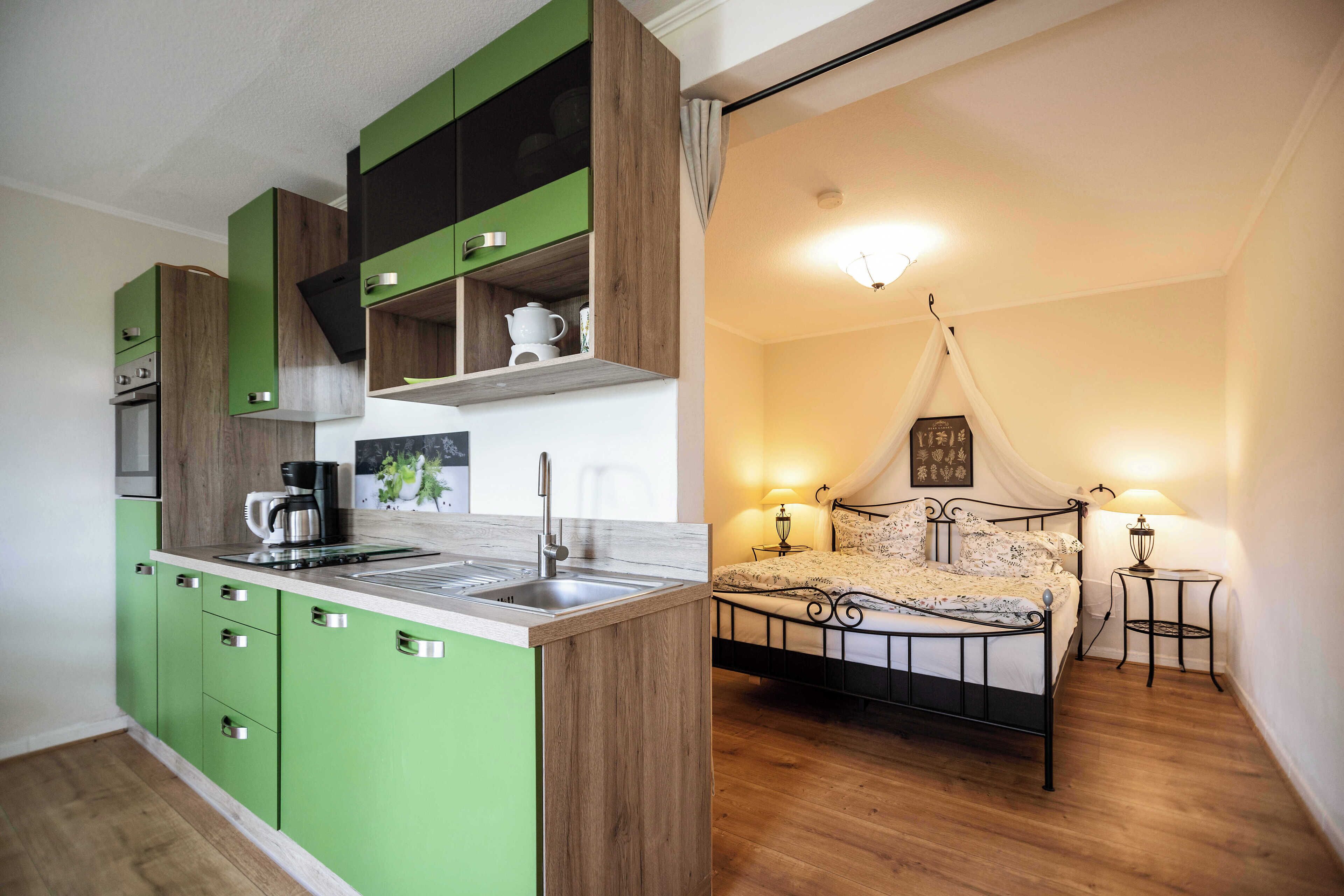 A modern kitchen with green cabinets and a wooden countertop, a bed with a canopy, and two bedside lamps.