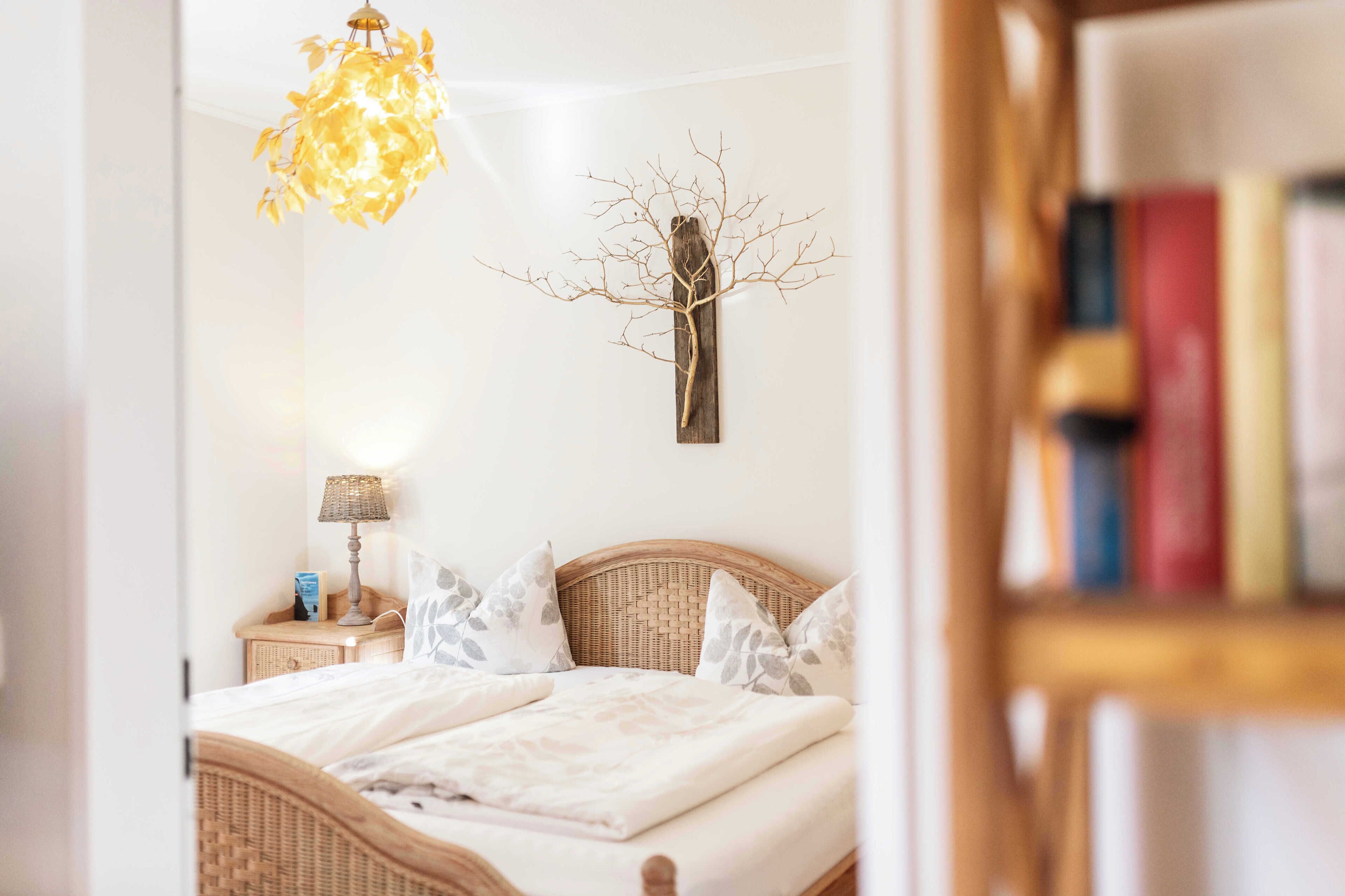 Une chambre à coucher comprenant un lit, une table de chevet, une lampe, une décoration murale en forme d’arbre et une bibliothèque.