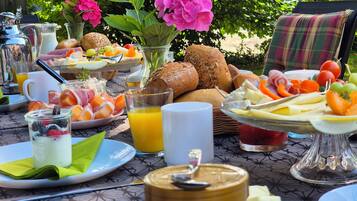 A breakfast table with various food items, a glass of orange juice, and a vase with flowers.