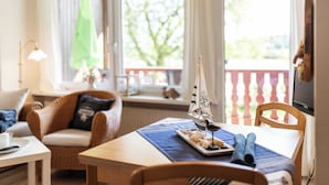 A cozy room with a wooden table, a chair, a small sailboat model, and a window with a view of greenery. - Immenhagen (Malente)
