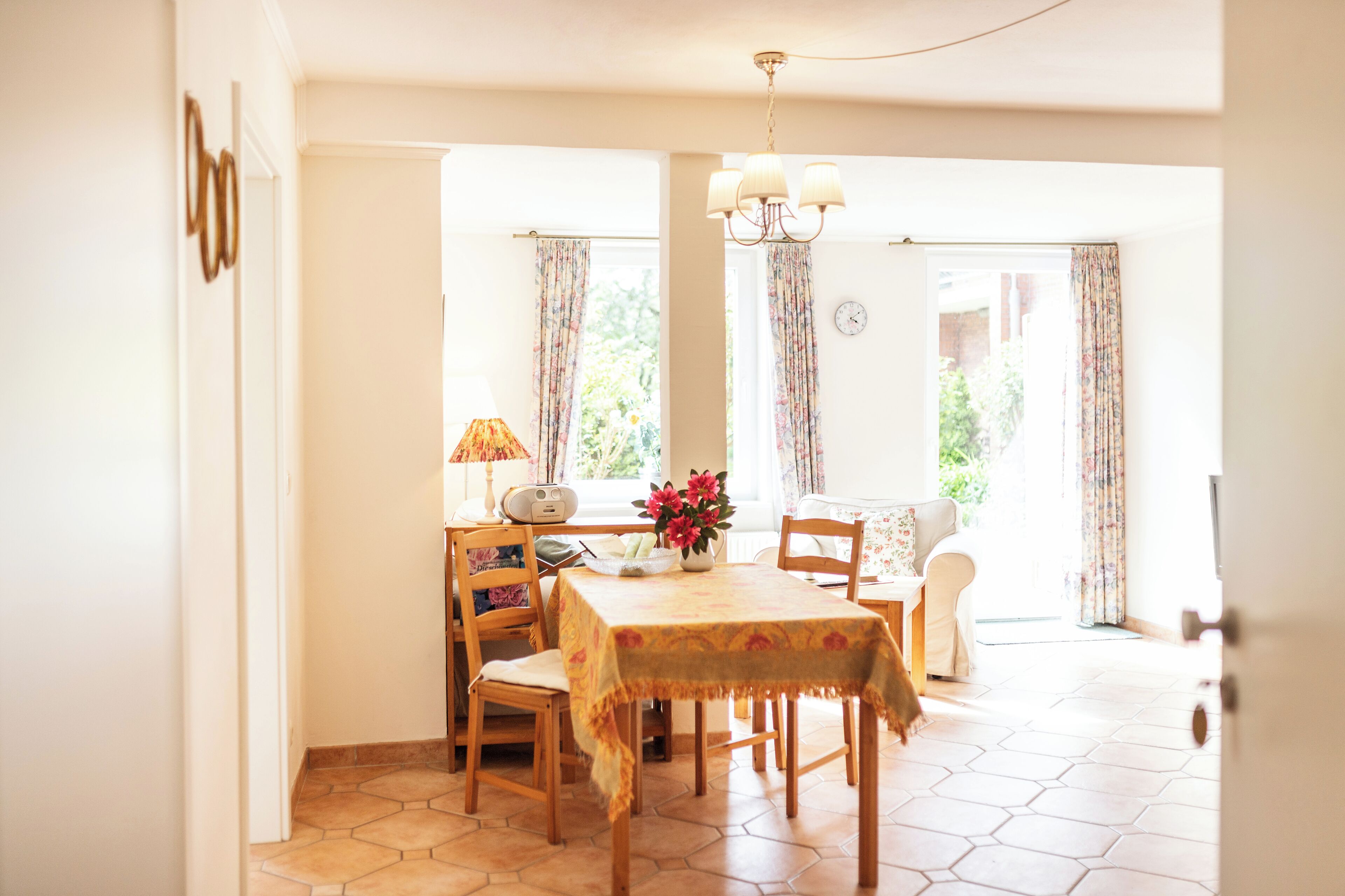 Un coin repas avec une table dressée pour quatre personnes, des chaises, une lampe et un vase de fleurs.