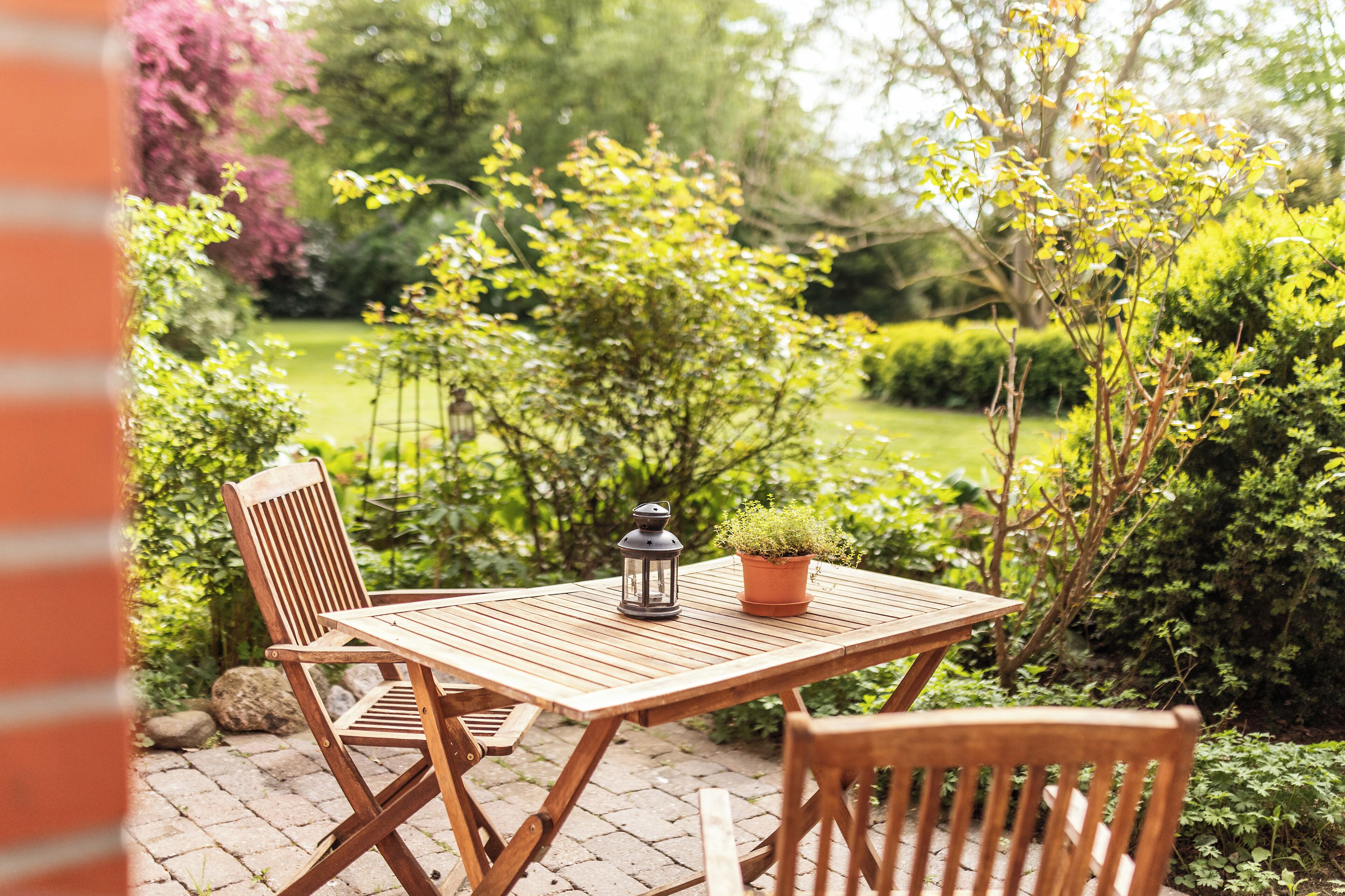An outdoor wooden table with chairs, a lantern, and a potted plant in a garden setting.