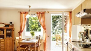 A kitchen with wooden cabinets, a dining table with chairs, and a view of the outdoors. - Immenhagen (Malente)