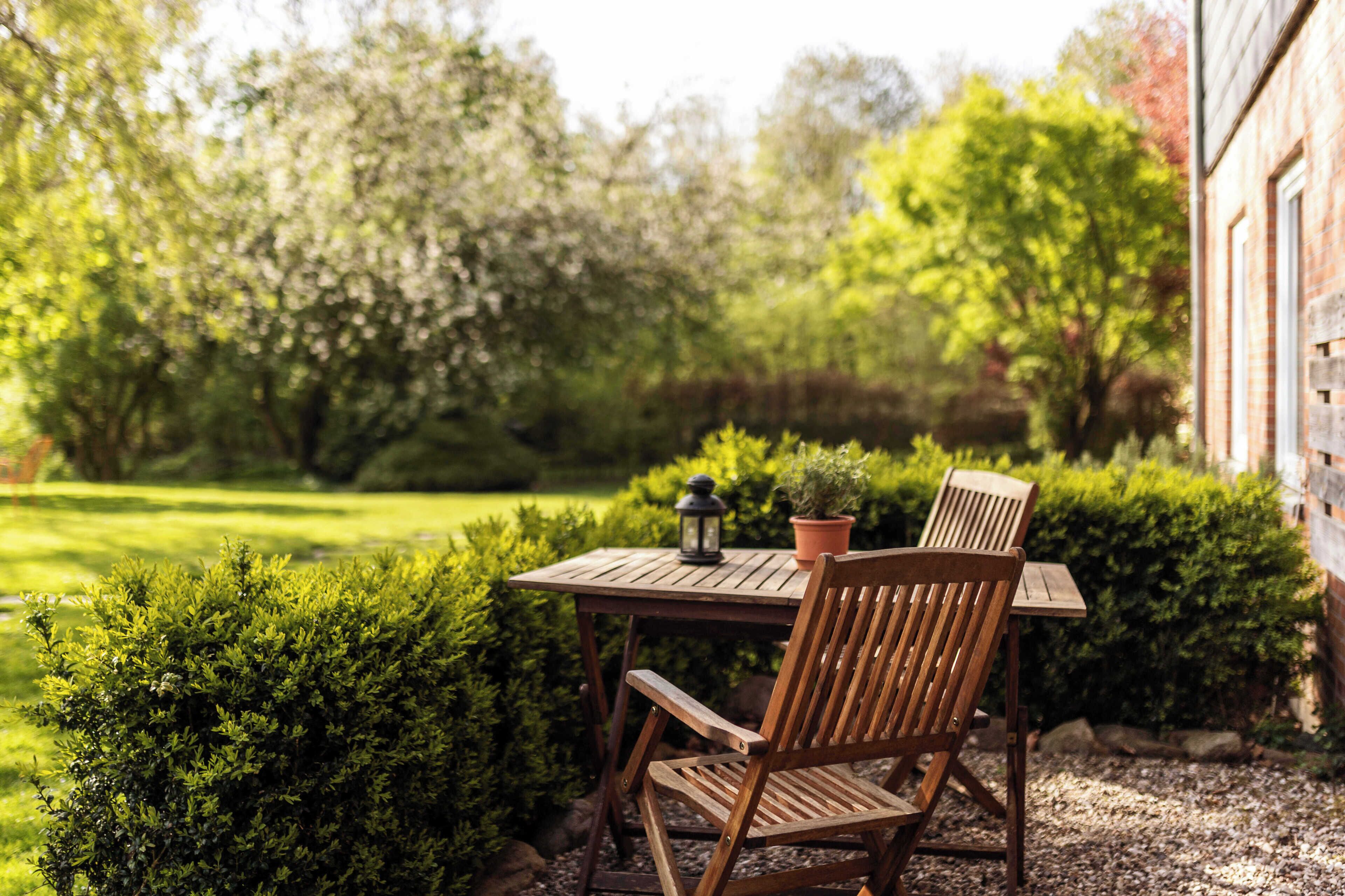 Een houten tafel met twee stoelen in een tuin, met een bloempot en een lantaarn op tafel.