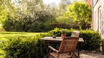 Een houten tafel met twee stoelen in een tuin, met een bloempot en een lantaarn op tafel.