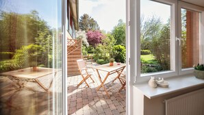 A patio with a table and chairs, a potted plant, and a view of a garden through a glass door. - Immenhagen (Malente)