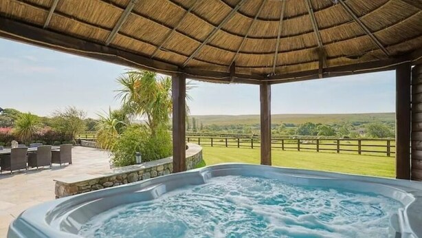 Un bain à remous doté d’un toit de chaume et offrant une vue sur un paysage verdoyant.