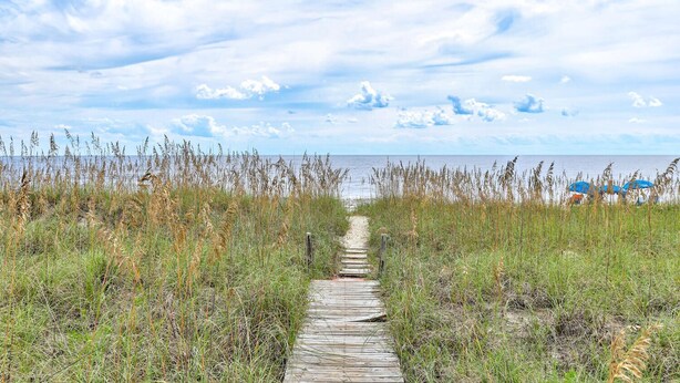 A wooden pathway leading to a beach with tall grasses and a clear sky. - Granny's Place - Oceanfront Home with Private beach access & Large Decks (Carolina Beach)