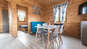 Interior de una cabaña de madera con una mesa de comedor, sillas, un sofá, una cama y una zona de cocina.