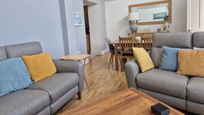A modern living room with two grey sofas, a wooden coffee table, and a dining area with a wooden table and chairs. - Spacious Modern Apartment with Sea Views in Prime Beachside Location (Westward Ho!)