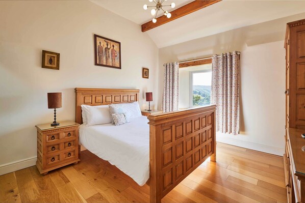 A bedroom with a wooden bed, a nightstand, a window with curtains, and a wooden ceiling.