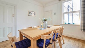 Ein Essbereich mit einem Holztisch und Stühlen, einer Vase mit Blumen und einem Fenster mit Vorhängen.