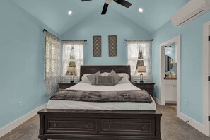 Ein Schlafzimmer mit einem dunkelholzbett, zwei Nachttischen mit Lampen, einem Deckenventilator und einer Tür zu einem Badezimmer.