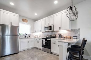 A modern kitchen with white cabinets, stainless steel appliances, and a granite countertop. - Live Oak Cabins-Sleeps 8 w/Hot-Tubs (Fredericksburg)