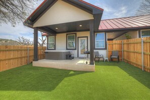A covered patio area with a hot tub, outdoor seating, and a wooden fence. - Live Oak Cabins-Sleeps 8 w/Hot-Tubs (Fredericksburg)