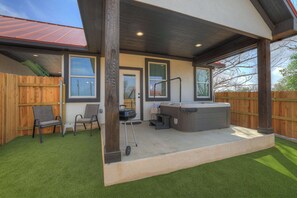 An outdoor patio with artificial grass, a hot tub, and two chairs.