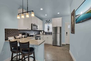 A modern kitchen with white cabinets, a stainless steel refrigerator, and a bar area with stools.
