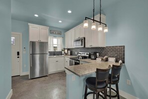 Una cocina moderna con armarios blancos, un refrigerador de acero inoxidable, un microondas y una isla de encimera de granito con taburetes de bar.