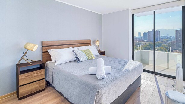 Ein modernes Schlafzimmer mit einem großen Bett, Nachttischen aus Holz, einem Balkon mit Blick auf die Stadt und einer Stadtansicht durch das Fenster.