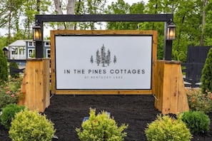 Une enseigne pour « In the Pines Cottages at Kentucky Lake », avec un design simple et une illustration représentant une forêt.