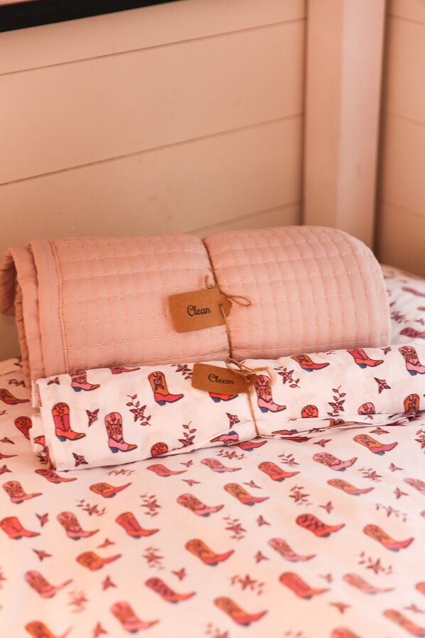 A neatly folded quilted blanket with a tag labeled "Clean" and a pillow with a floral pattern.