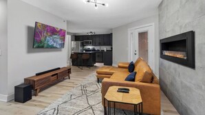 A modern living room with a sofa, coffee table, and TV. There is a kitchen in the background with a microwave and cabinets. - The Lofts of Downtown 540 N 2nd St, #207 (Clarksville)