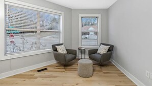 A corner room with two grey armchairs, a small round ottoman, and a window with blinds. - The Lofts of Downtown 540 N 2nd St, #207 (Clarksville)