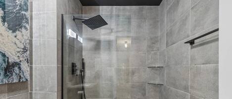 Un baño moderno con mampara de vidrio, un cabezal de ducha manual e iluminación empotrada en la pared.