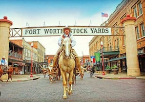 Une scène de rue avec une enseigne indiquant « FORT WORTH STOCK YARDS » et un attelage tiré par des chevaux au premier plan.
