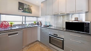 Een moderne keuken met roestvrijstalen apparatuur, grijze kasten en een raam met jaloezieën.