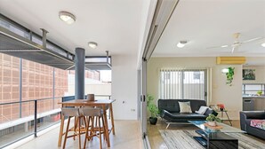 Een ruime woonkamer met een eettafel, stoelen, een bank en een salontafel. Er is een groot raam met uitzicht op het buiten.