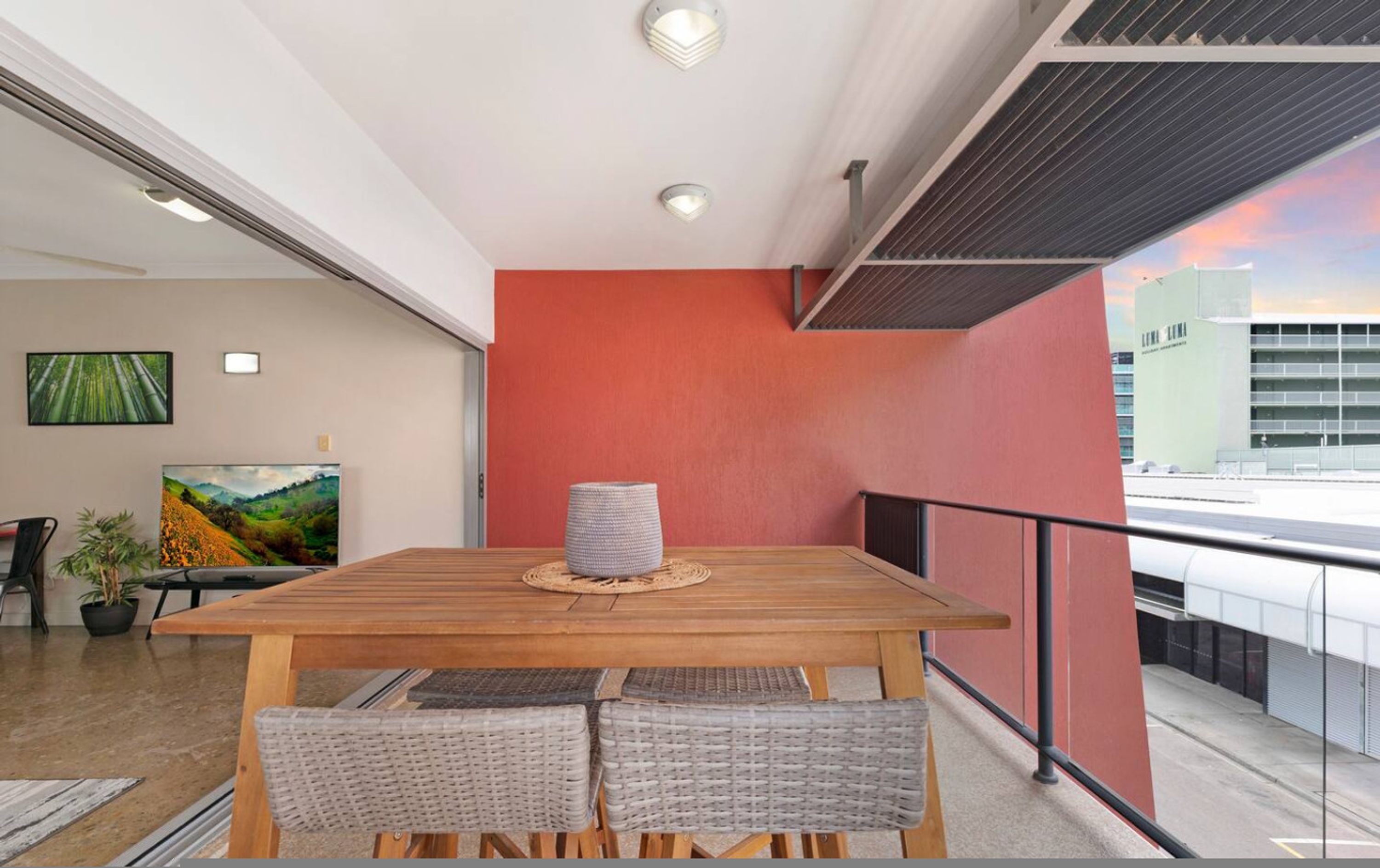 Ein moderner Essbereich mit Holztisch, Korbstühle, einer roten Akzentwand und Blick auf die Stadt.