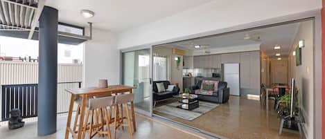 A modern living space with a dining area, a sofa, and a kitchen in the background.