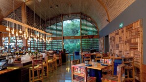Ein Restaurant mit Holztischen, hängenden Lampen und großen Fenstern.