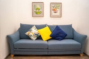 A grey sofa with three cushions, two framed artworks above it, and a wooden floor.
