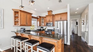 A modern kitchen with wooden cabinets, a central island with bar stools, stainless steel appliances, and pendant lighting.