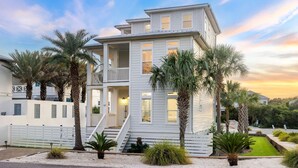A two-story house with a balcony, surrounded by palm trees and a well-maintained lawn.