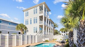 A two-story building with a pool, outdoor seating, and a white fence.