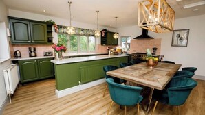 Una cocina moderna con armarios verdes, una mesa de comedor de madera, sillas color turquesa y lámparas colgantes.