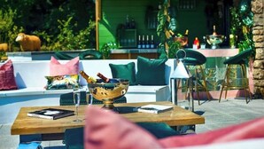 Un área de estar al aire libre con una mesa de madera, un cuenco y un libro. Se ve una pared verde y una zona de bar al fondo.